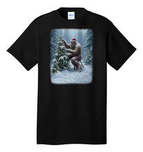 Load image into Gallery viewer, Bigfoot Christmas T-Shirt Lonely Sasquatch Decorating a Christmas Tree Wearing a Santa Hat in a Forest With Snow